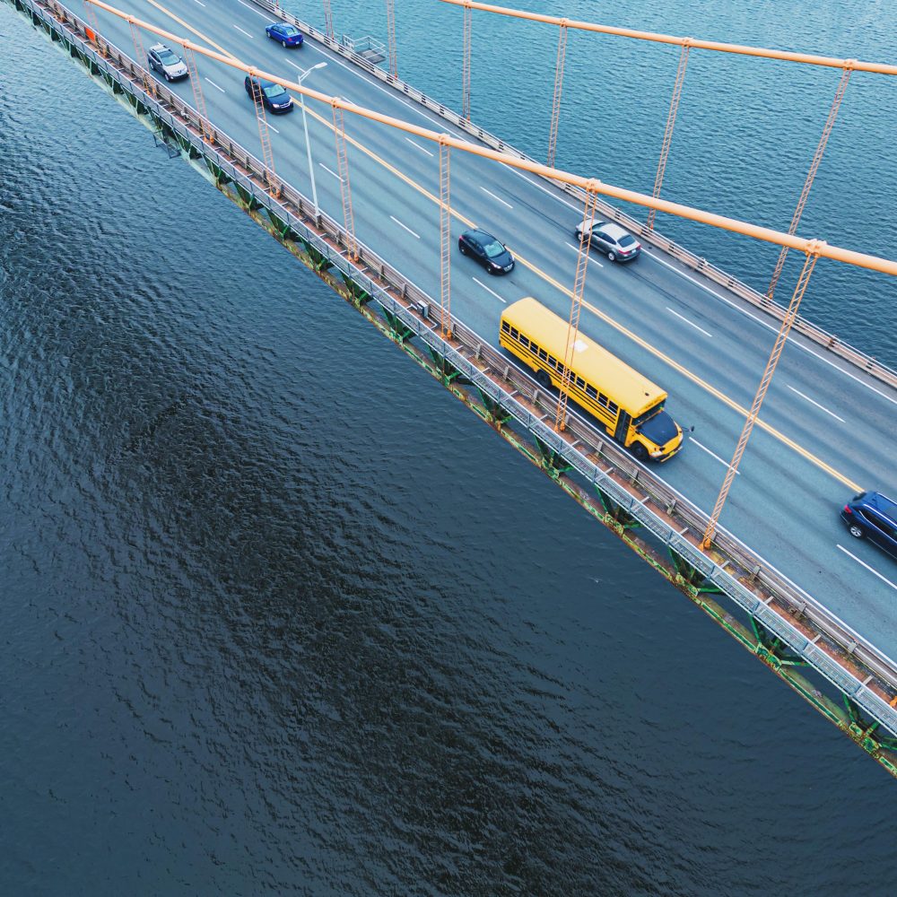 Aerial view of a school bus crossing a suspension bridge at afternoon dismissal.